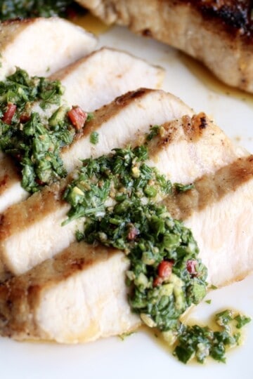 slices of a chimichurri pork chop are fanned out on a plate topped with a line of bright green chimichurri sauce