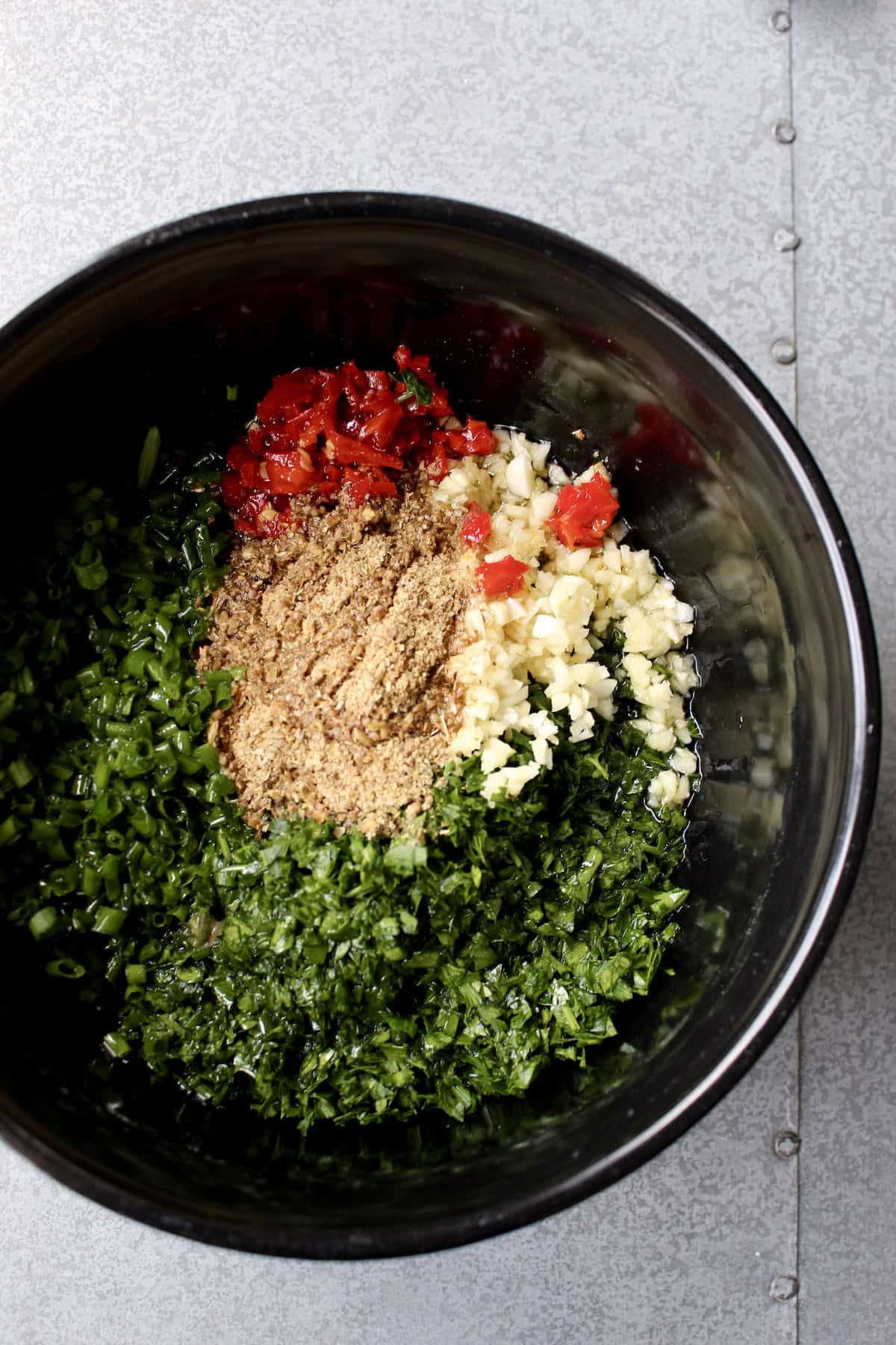 the ground spices, olive oil, and vinegar are added to the bowl containing all of the minced ingredients