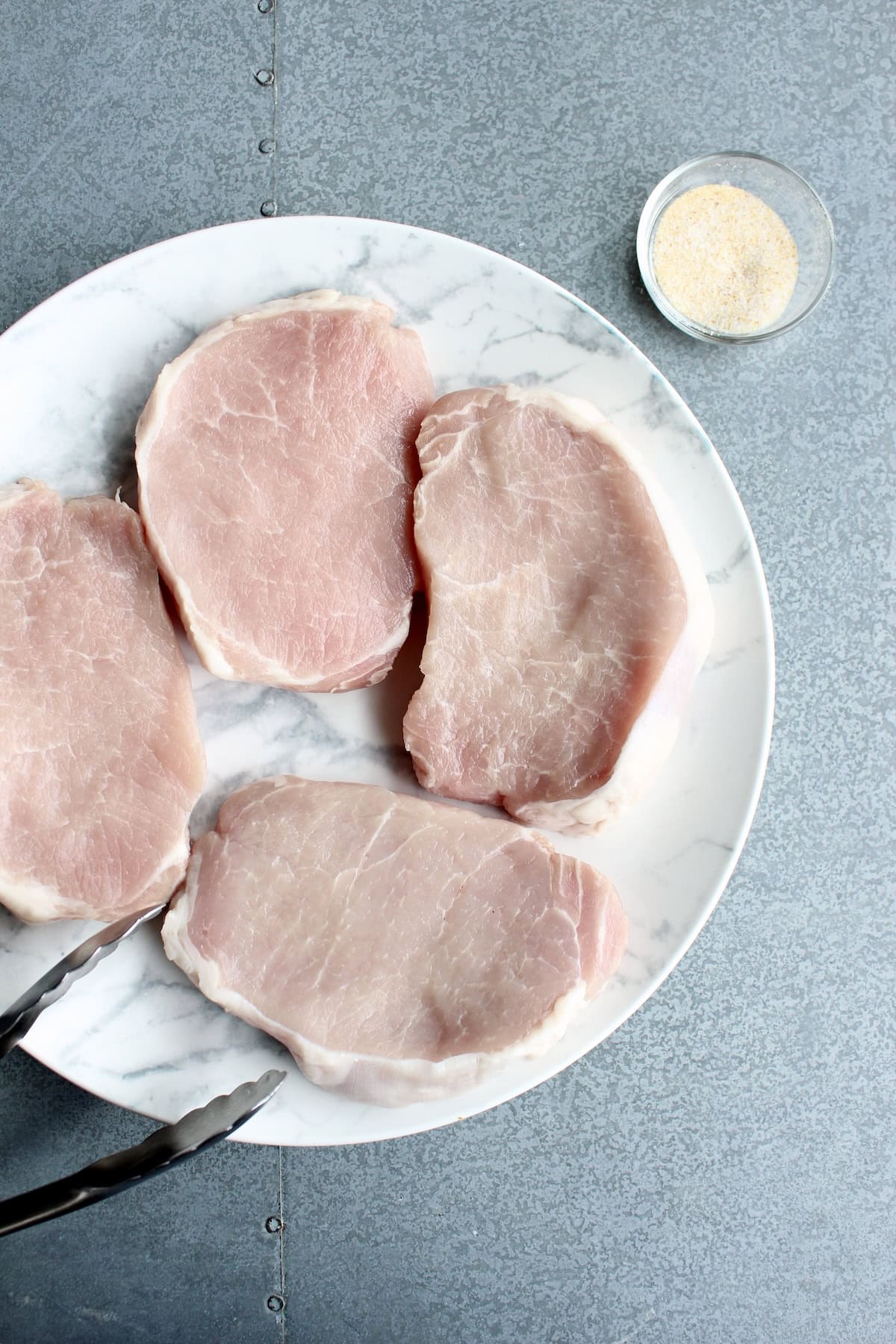 4 pork chops on a plate next to a small bowl of seasoning