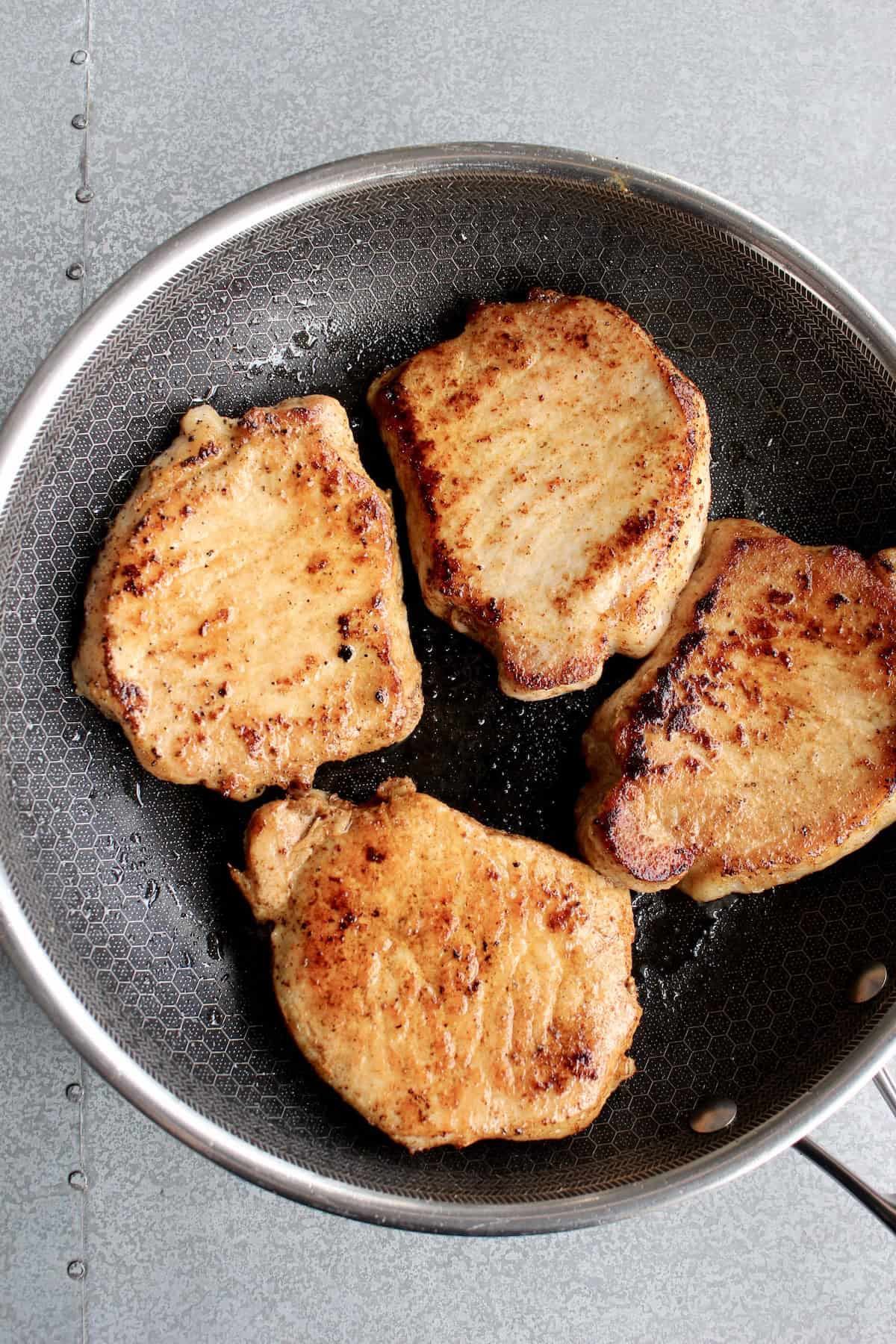 4 golden brown, fully cooked pork chops are arranged in a large skillet
