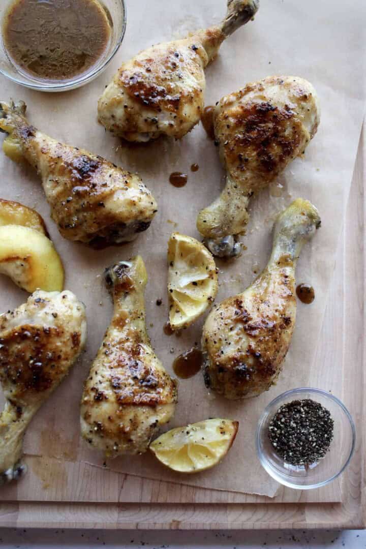 lemon pepper chicken legs on a wooden serving board are glistening with a coating of pan juices