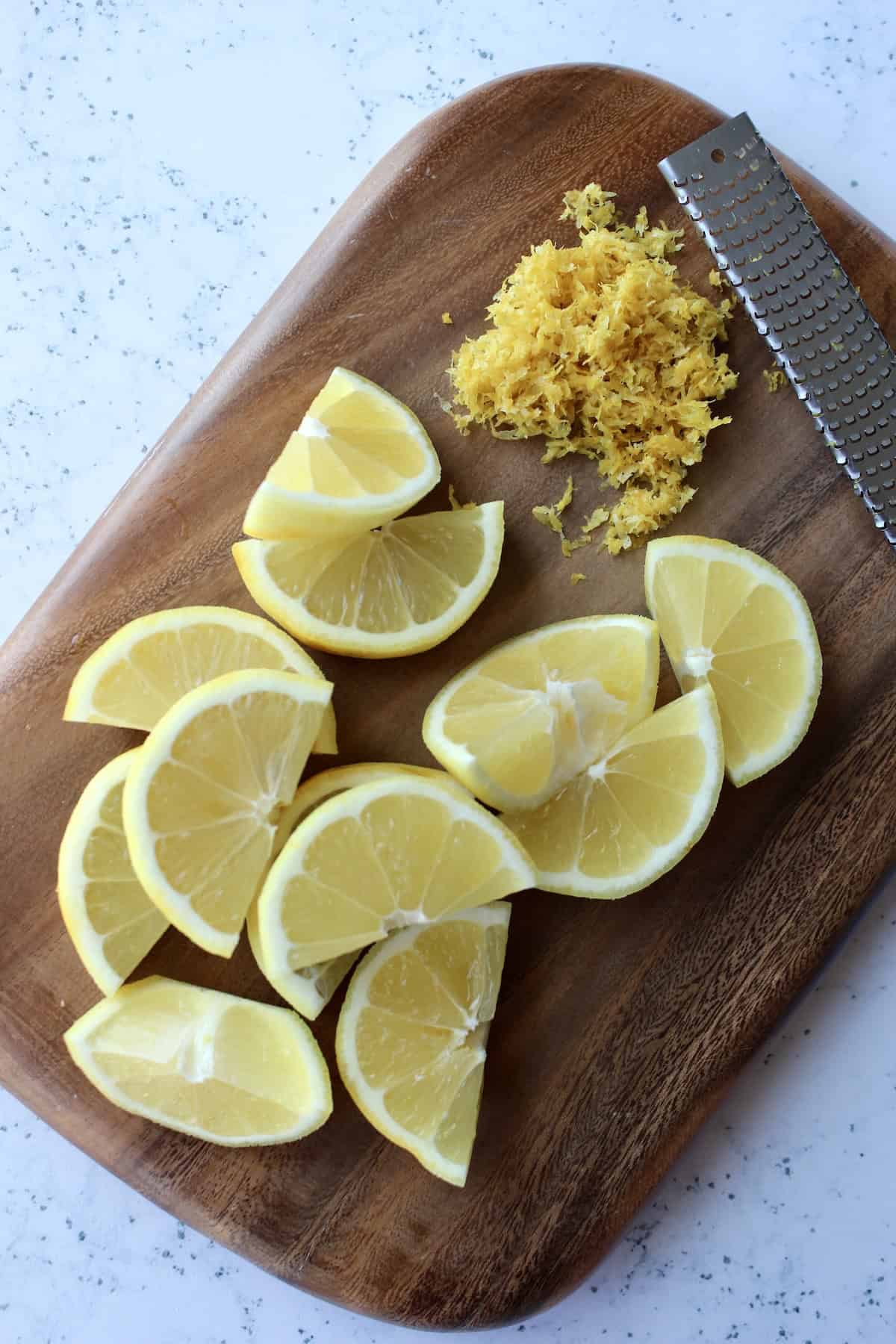 a small wooden cutting board with a pile of fresh lemon zest and thick lemon wedges