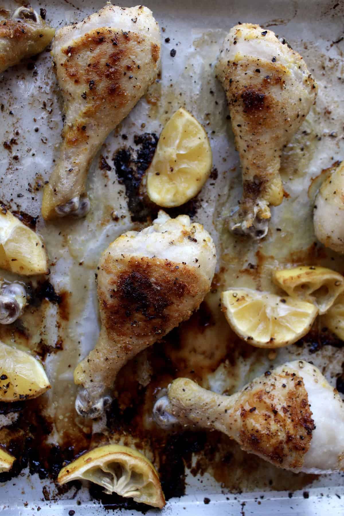 the cooked lemon pepper chicken legs have a deep brown coloring and the lemon wedges have carameliezd