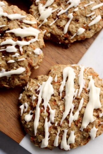 oatmeal carrot cake cookies are drizzled with cream cheese glaze and served on a marble and wooden board