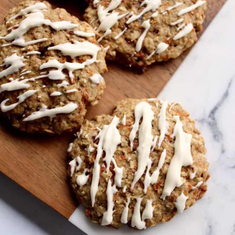 oatmeal carrot cake cookies are drizzled with cream cheese glaze and served on a marble and wooden board