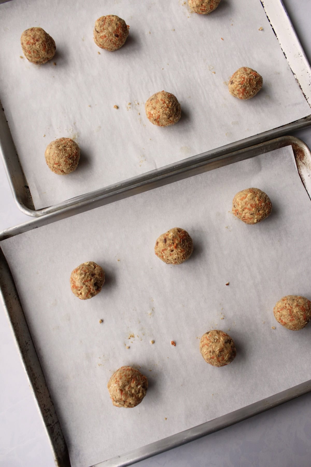12 portioned and rolled dough balls are arranged on 2 parchment paper lined baking sheets