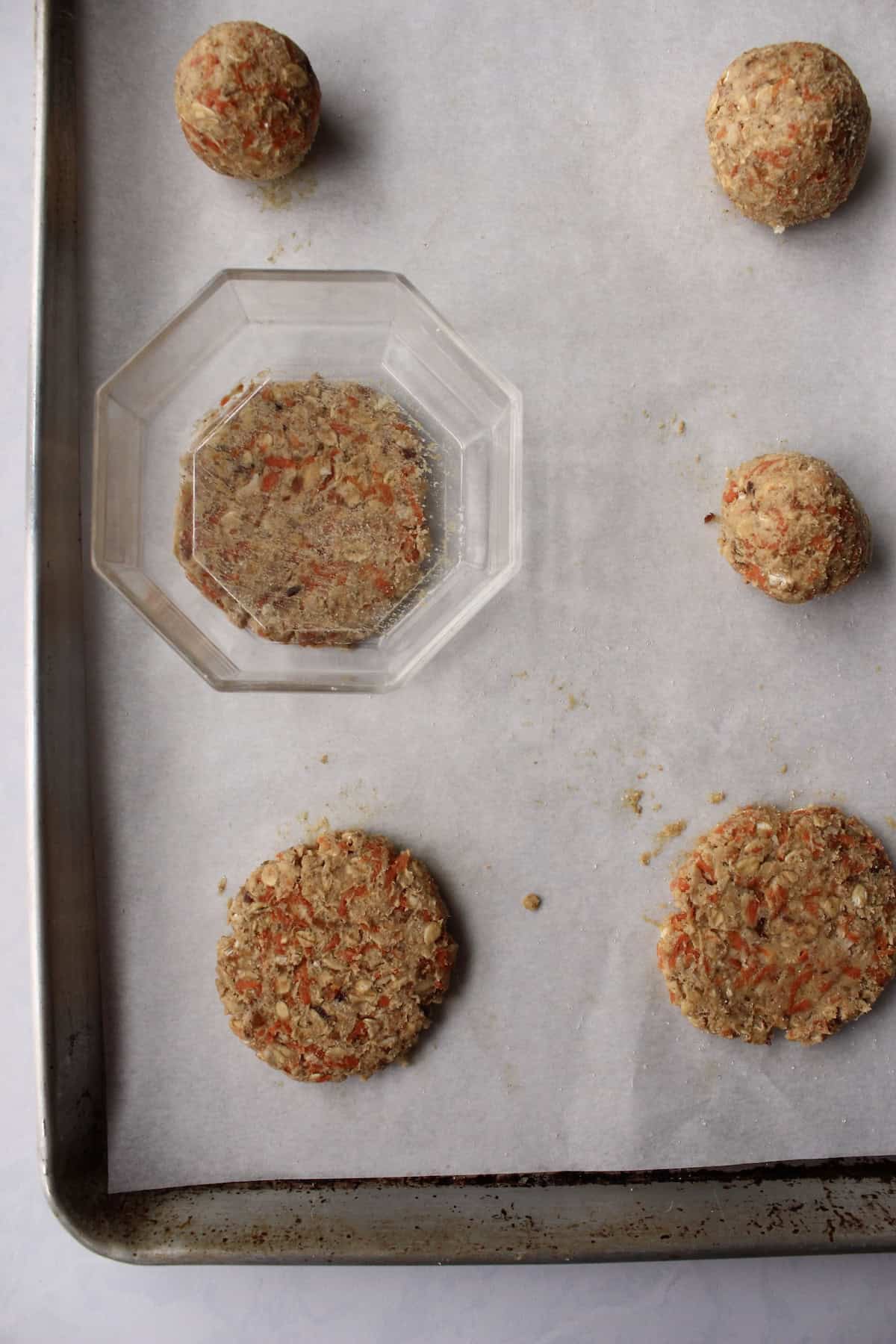 the dough balls are pressed down with a clear glass bowl, turning the balls into flat cookie patties