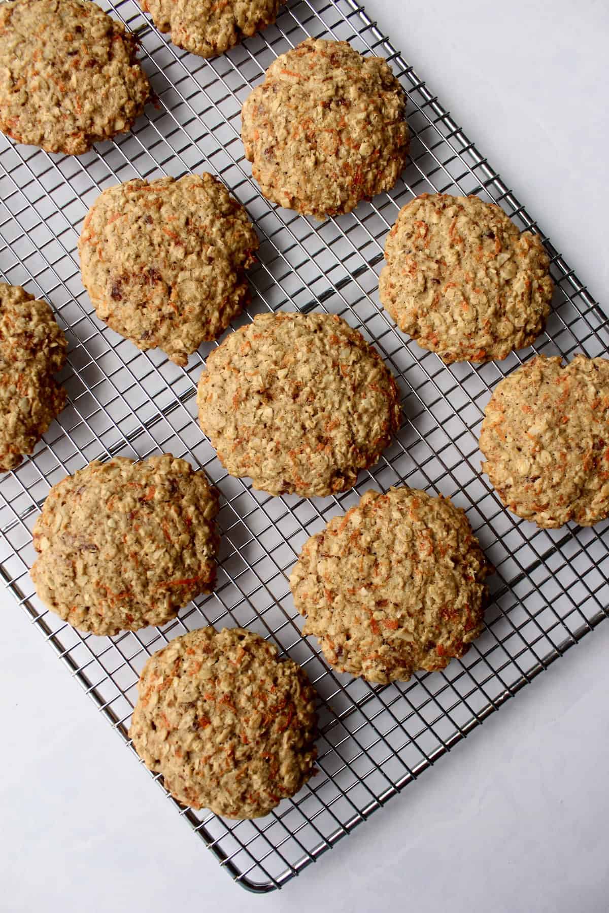 the baked oatmeal carrot cake cookies are arranged on a wire cooling rack on the countertop