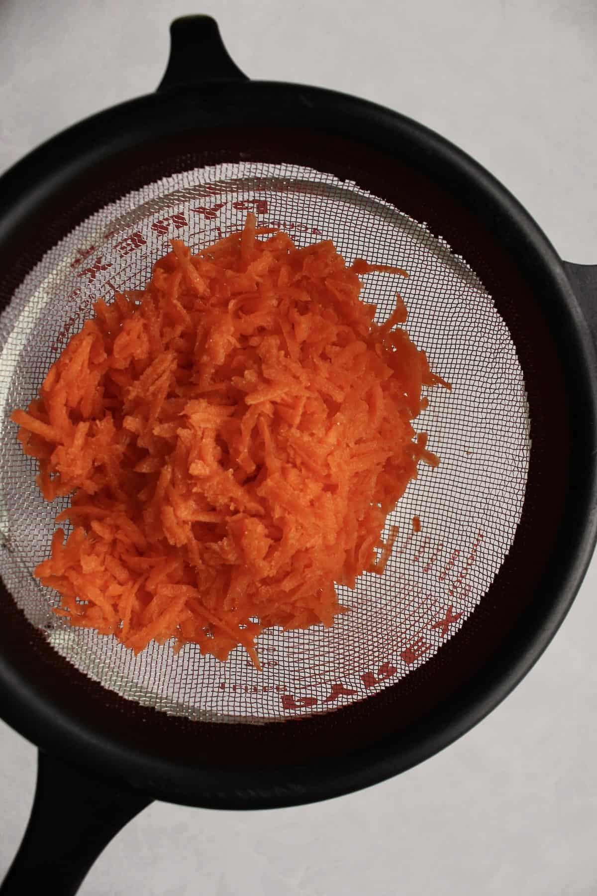 a strainer containing shredded carrots is set over a glass pitcher