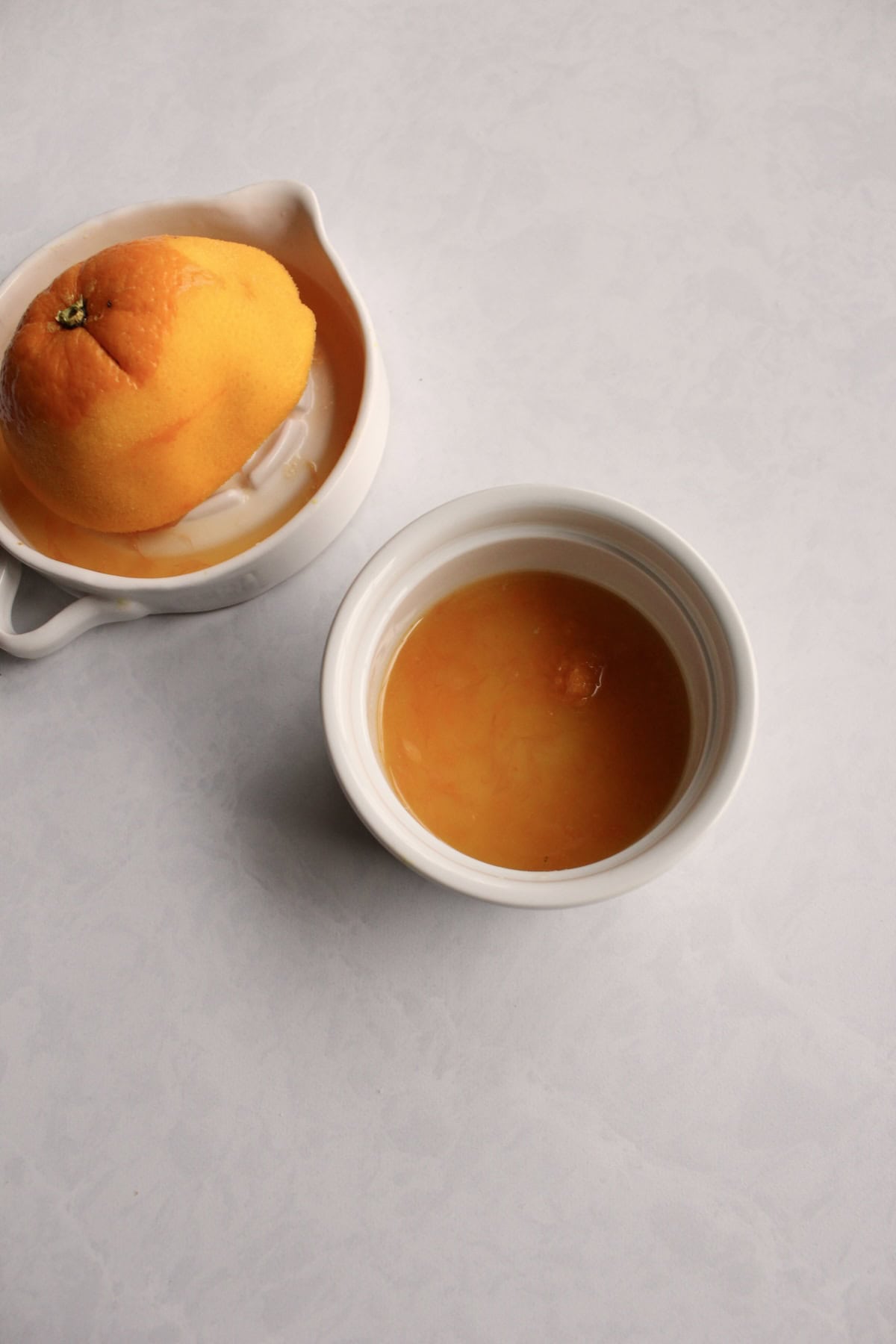 a small bowl of orange juice and zest sits next to a squeezed orange half
