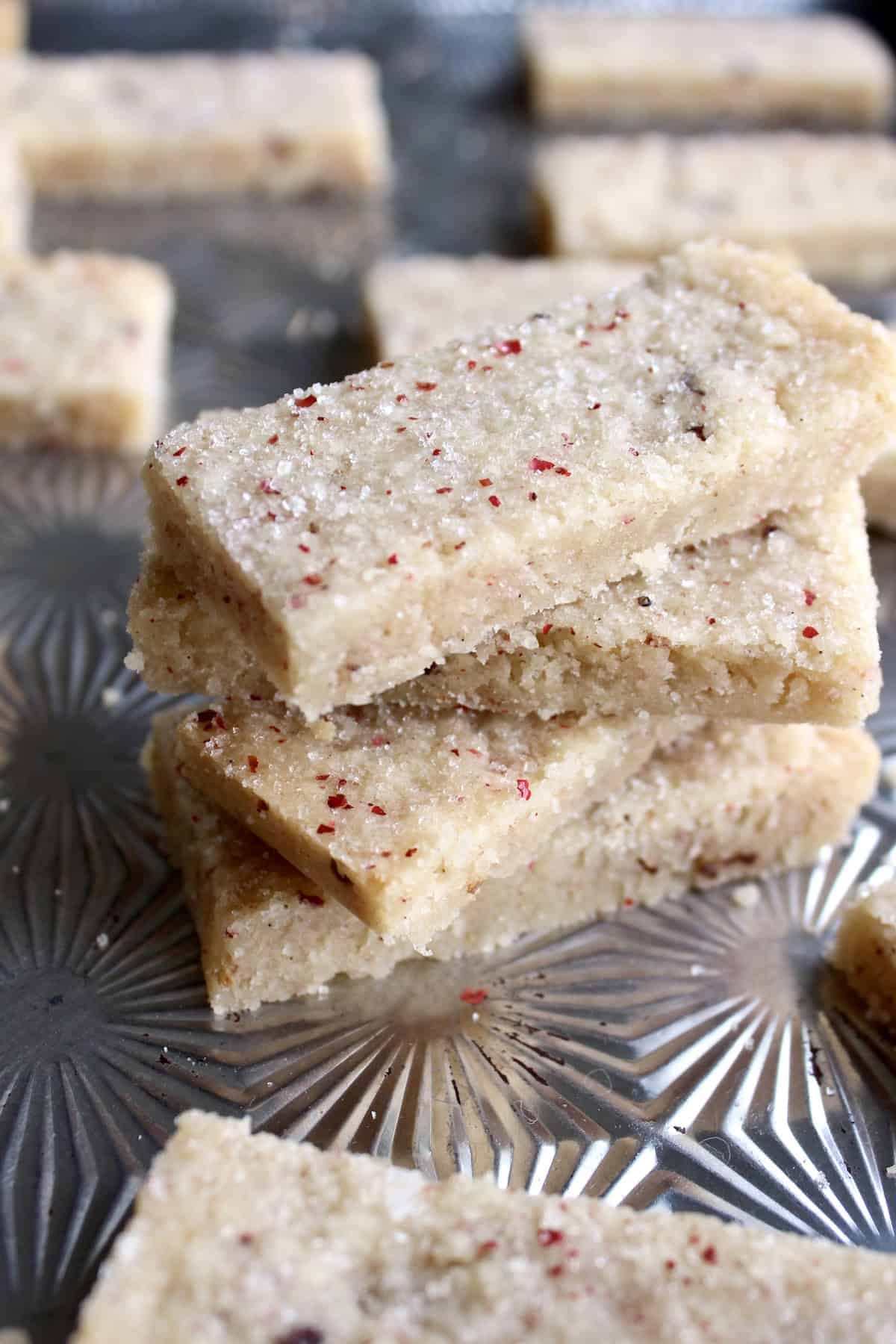bar shaped pink peppercorn shortbread cookies are stacked on a vintage baking sheet