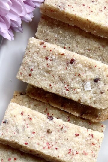 rectangular pink peppercorn shortbread cookies are stacked on a white platter near pink flowers