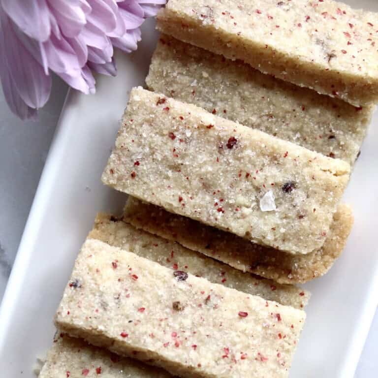 rectangular pink peppercorn shortbread cookies are stacked on a white platter near pink flowers