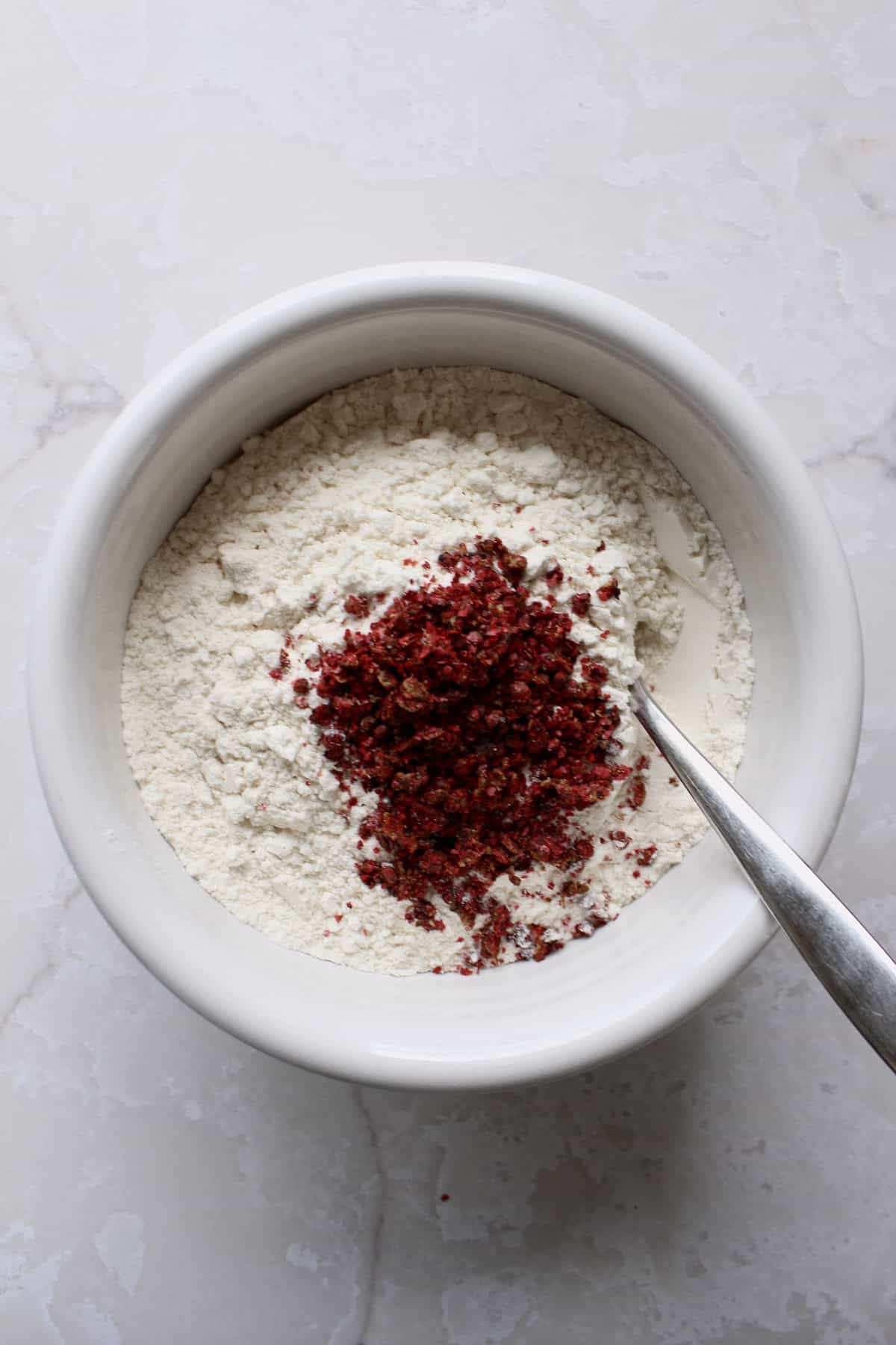 a pile of crushed pink peppercorns is added to a bowl of all-purpose flour