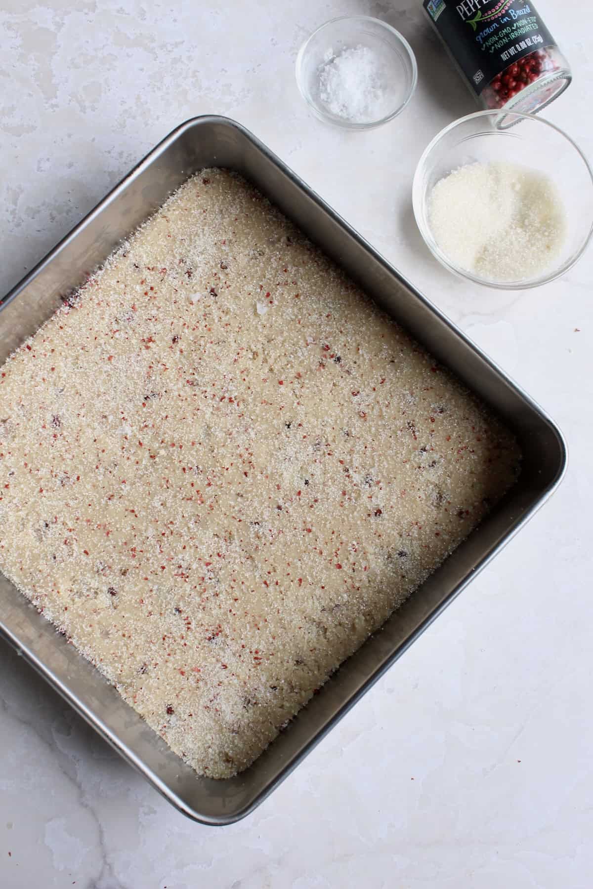 the surface of the unbaked pink peppercorn shortbread cookie dough is sprinkled with pink peppercorn flakes, flaky salt, and granulated sugar