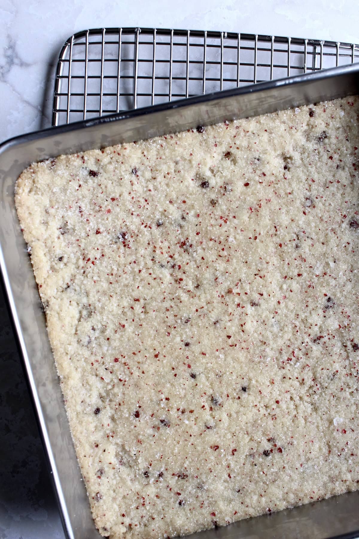 the pan of baked shortbread cookies is removed from the oven, showing a smooth, dry surface and lightly golden edges