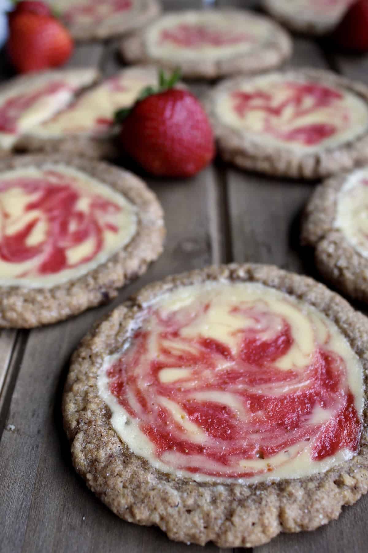 strawberry cheesecake cookies are arranged on a wooden board with fresh strawberries