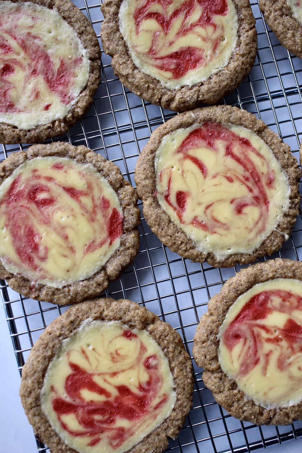 the baked strawberry cheesecake cookies are arranged on a wire cooling rack.