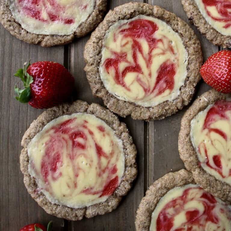 strawberry cheesecake cookies have a sugary graham cracker dough filled with ivory cheesecake filling and swirls of red strawberry sauce.