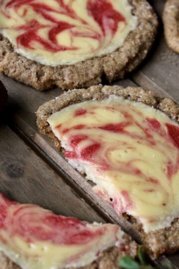 a halved strawberry cheesecake cookie is set on a wooden board along with several whole cookies and a few fresh strawberries