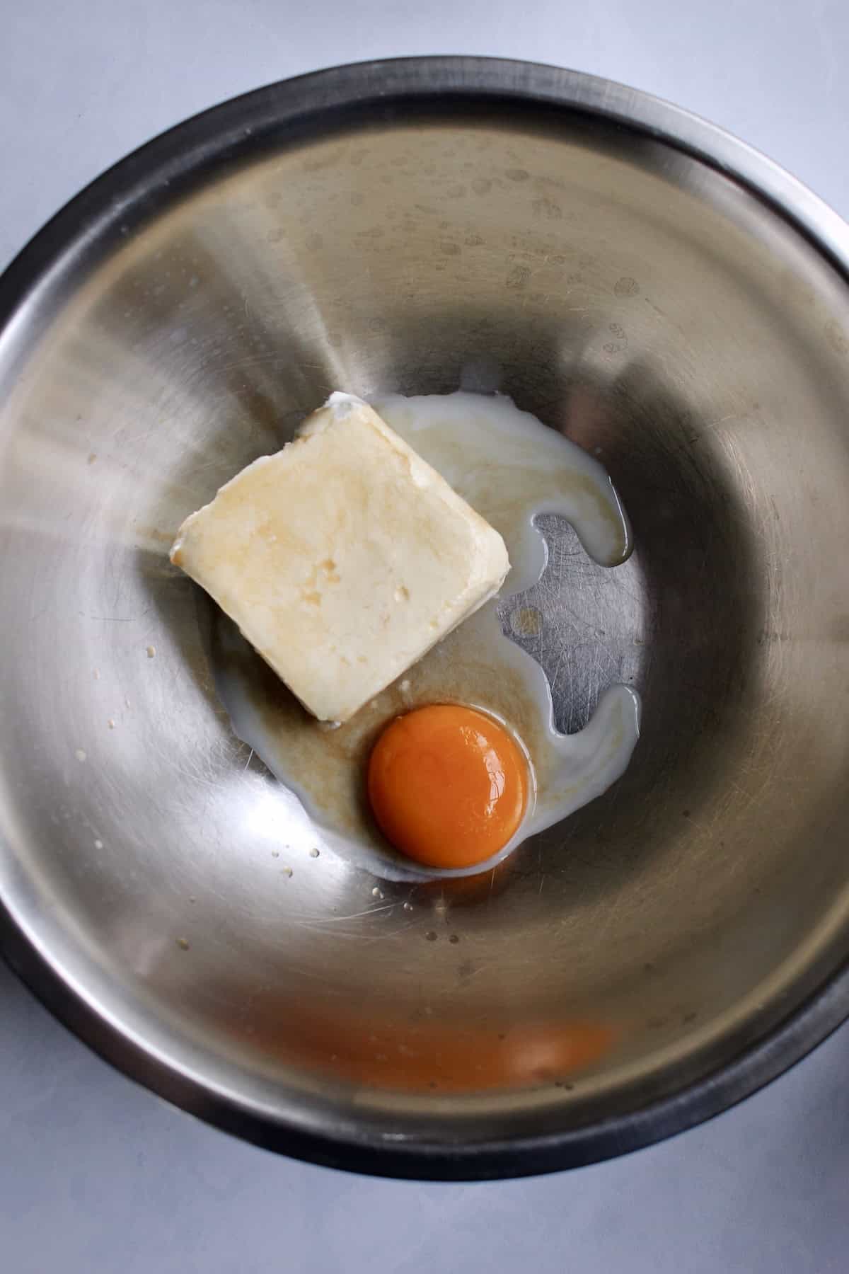 a large mixing bowl containing cream cheese, egg yolk, oat milk, and vanilla.