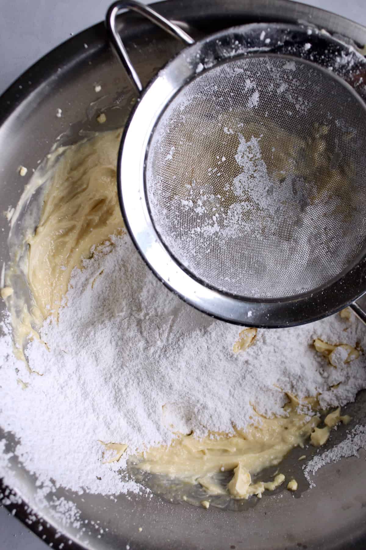 dry ingredients are sifted through a fine mesh strainer into the cream cheese mixture.