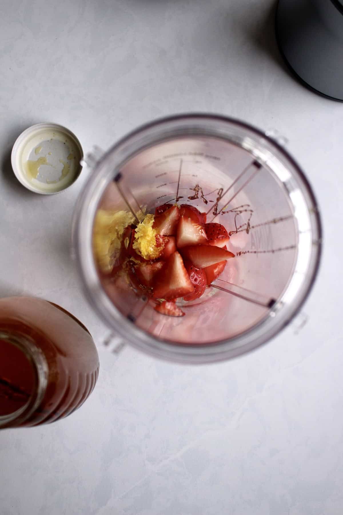 honey is added to a blender cup filled with the strawberries and lemon zest.