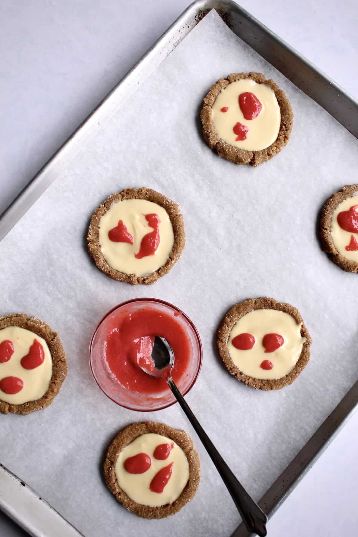 dots of strawberry sauce are dribbled on the surface of each cheesecake filled cookie.