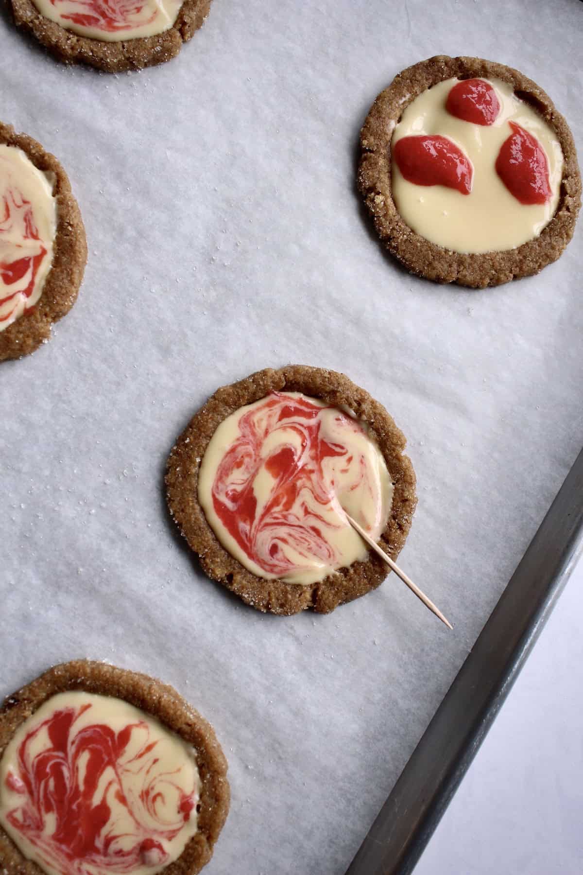 a toothpick is dragged through the strawberry dollops, swirling them into the cheesecake filling.
