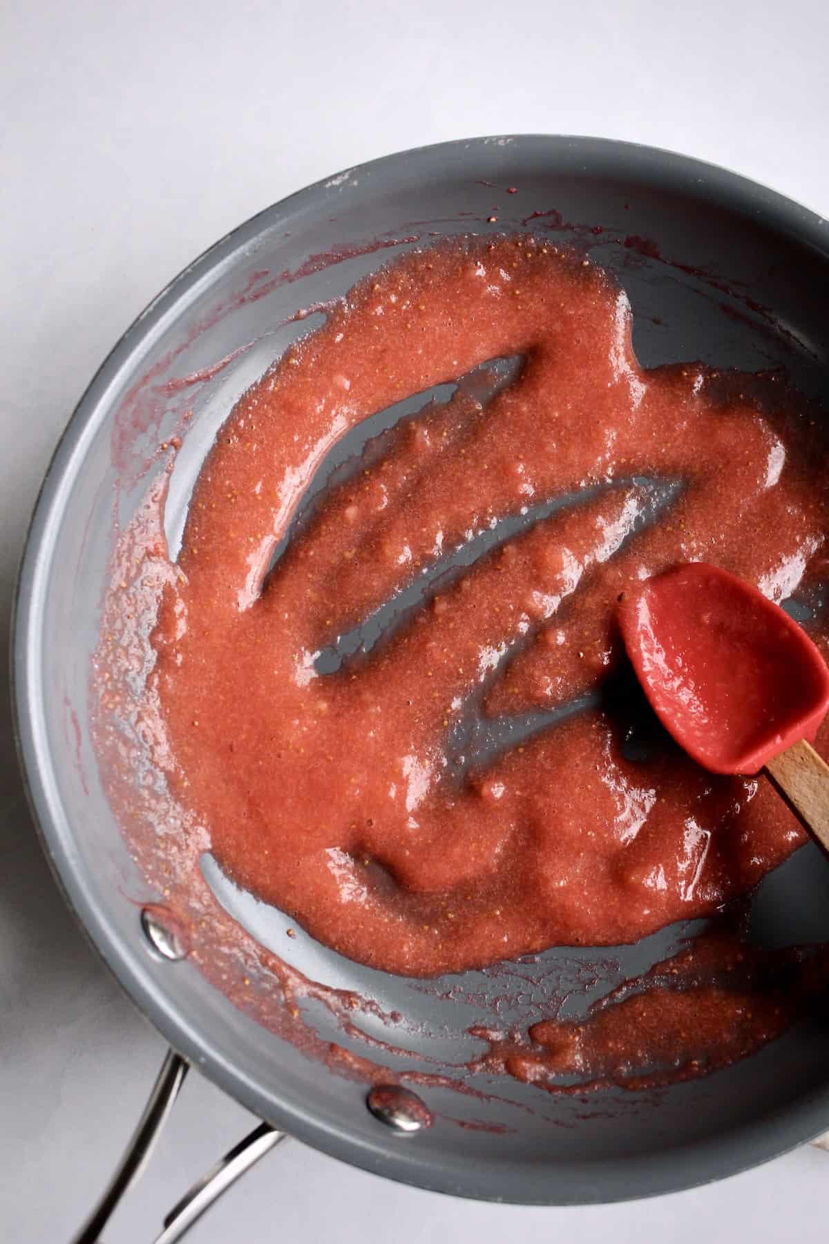 the cooked strawberry sauce has thickened in texture and darkened slightly in color.