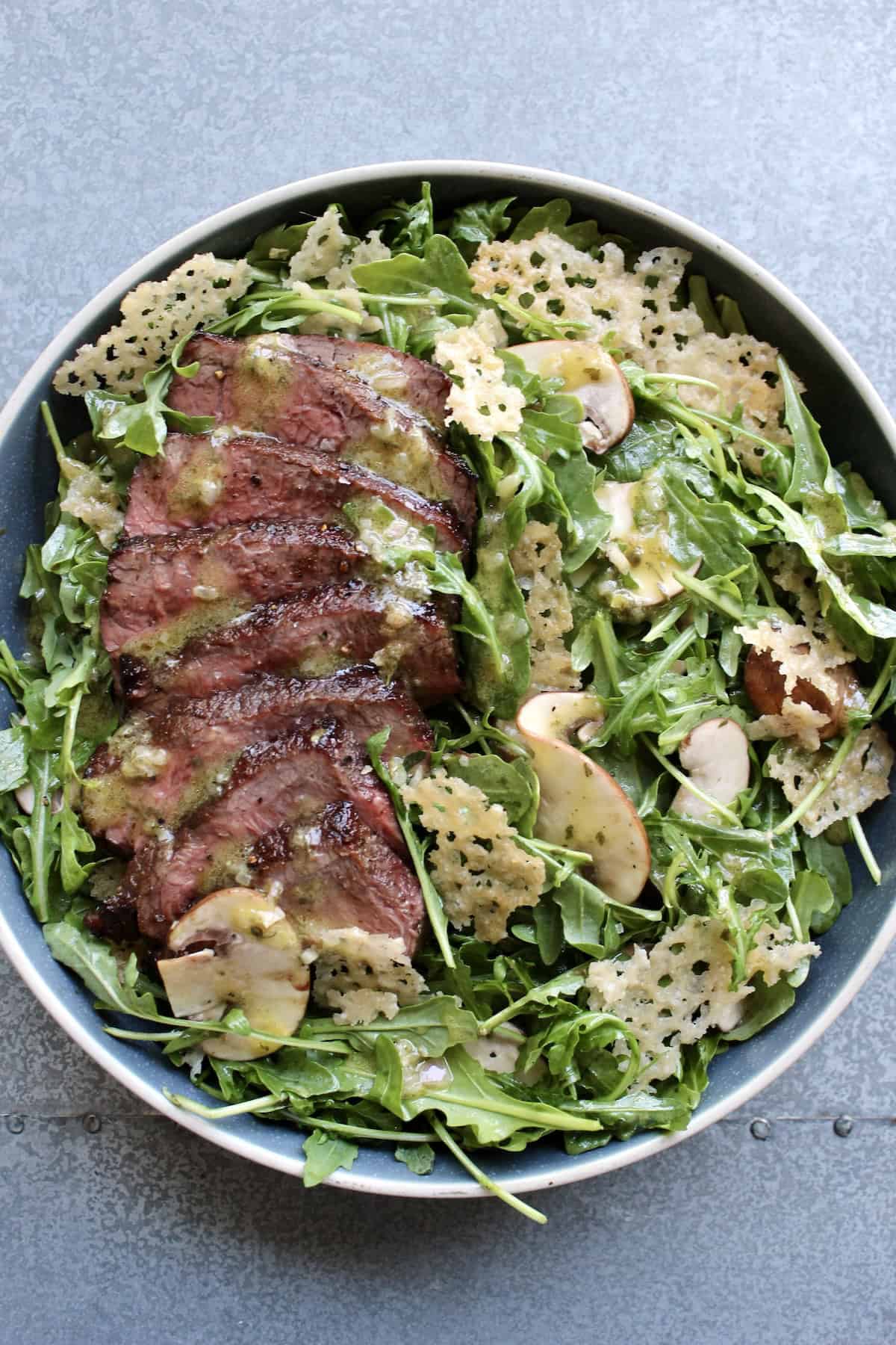 thinly sliced steak is added to the salad, drizzled with juices, dressing, and parmesan crisps