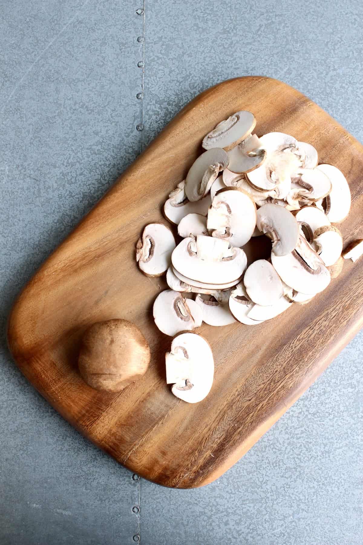 cremini mushrooms are thinly sliced on a wooden cutting board