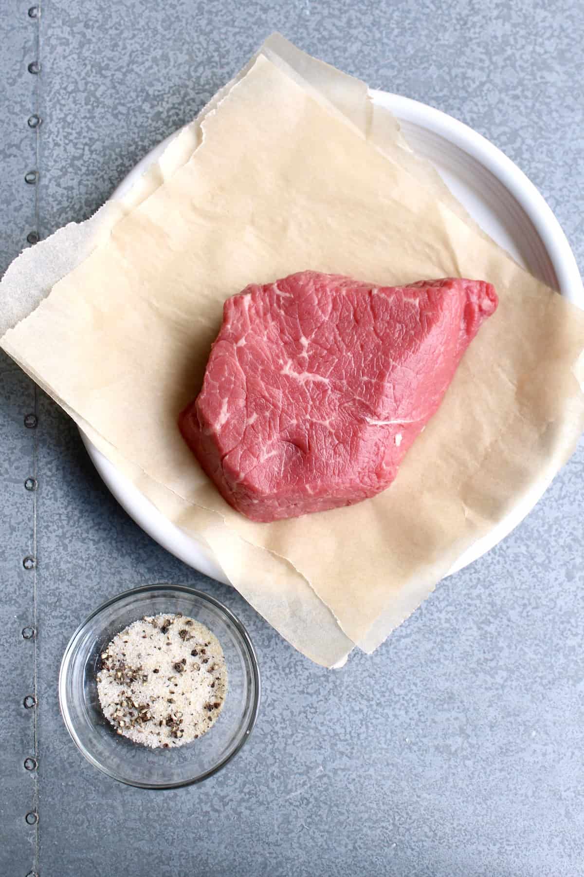 a petite sirloin steak sits on butcher paper next to a small bowl of spice mixture