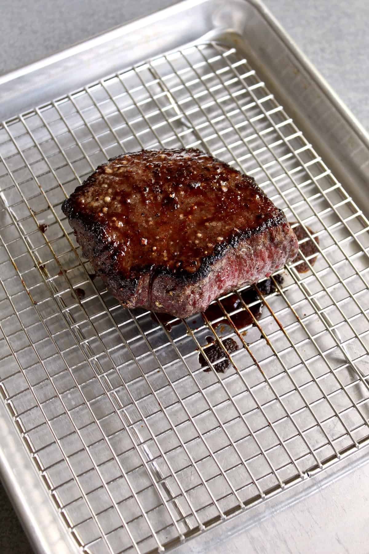 a deeply golden-brown, cooked steak rests on a wire rack set into a baking sheet.