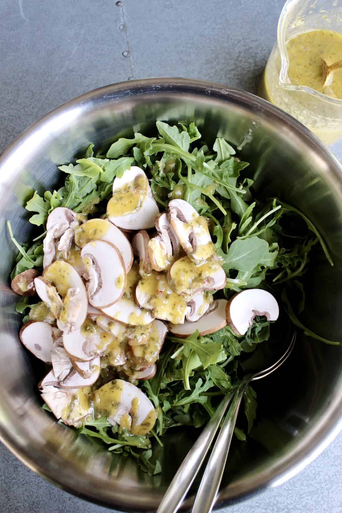salad ingredients are combined in a stainless steel mixing bowl and drizzled with dressing