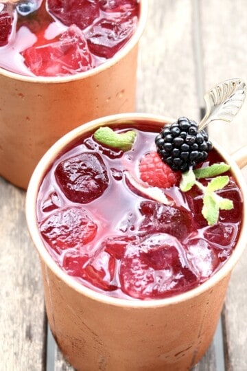 two berry moscow mules in copper mugs are on an outdoor patio table