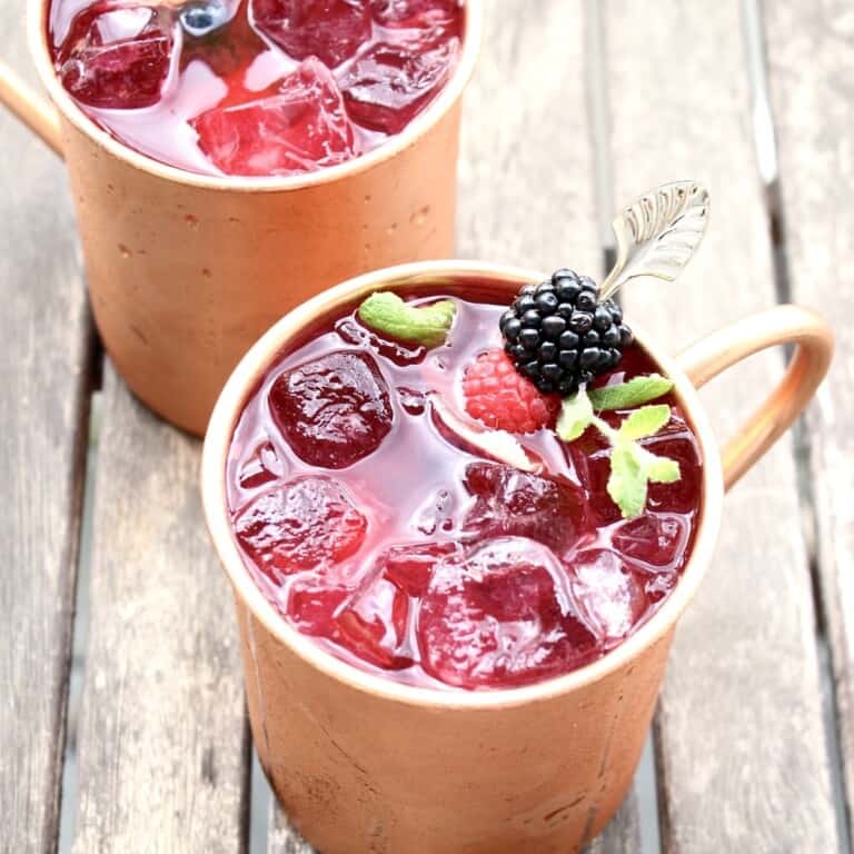 two berry moscow mules in copper mugs are on an outdoor patio table