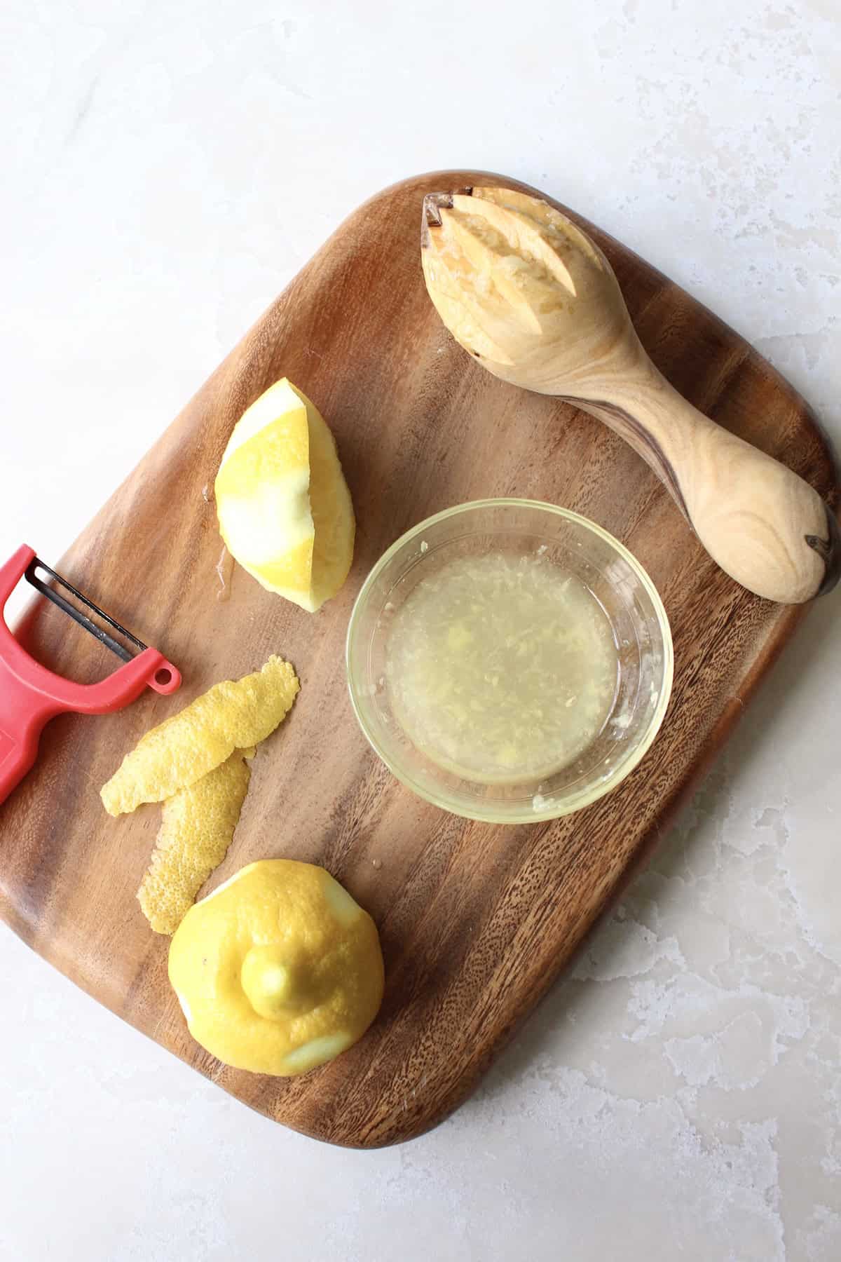 lemons on a small cutting board are in various stages of being juiced and peeled.
