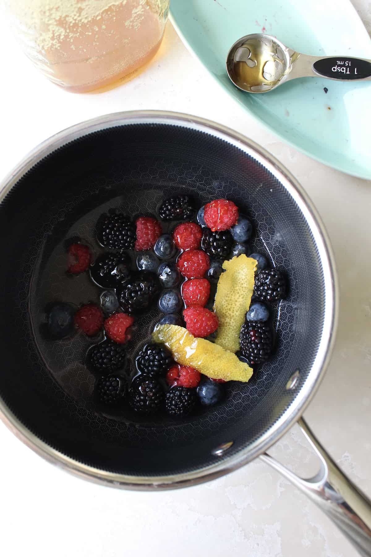 a small pot containing fresh berries, lemon peel, and liquid ingredients