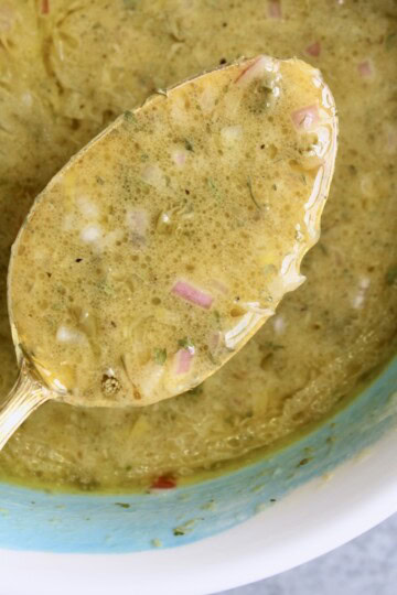 shallot lemon vinaigrette is spooned from a bowl, showing its thick texture with bits of shallot, capers, and herbs.
