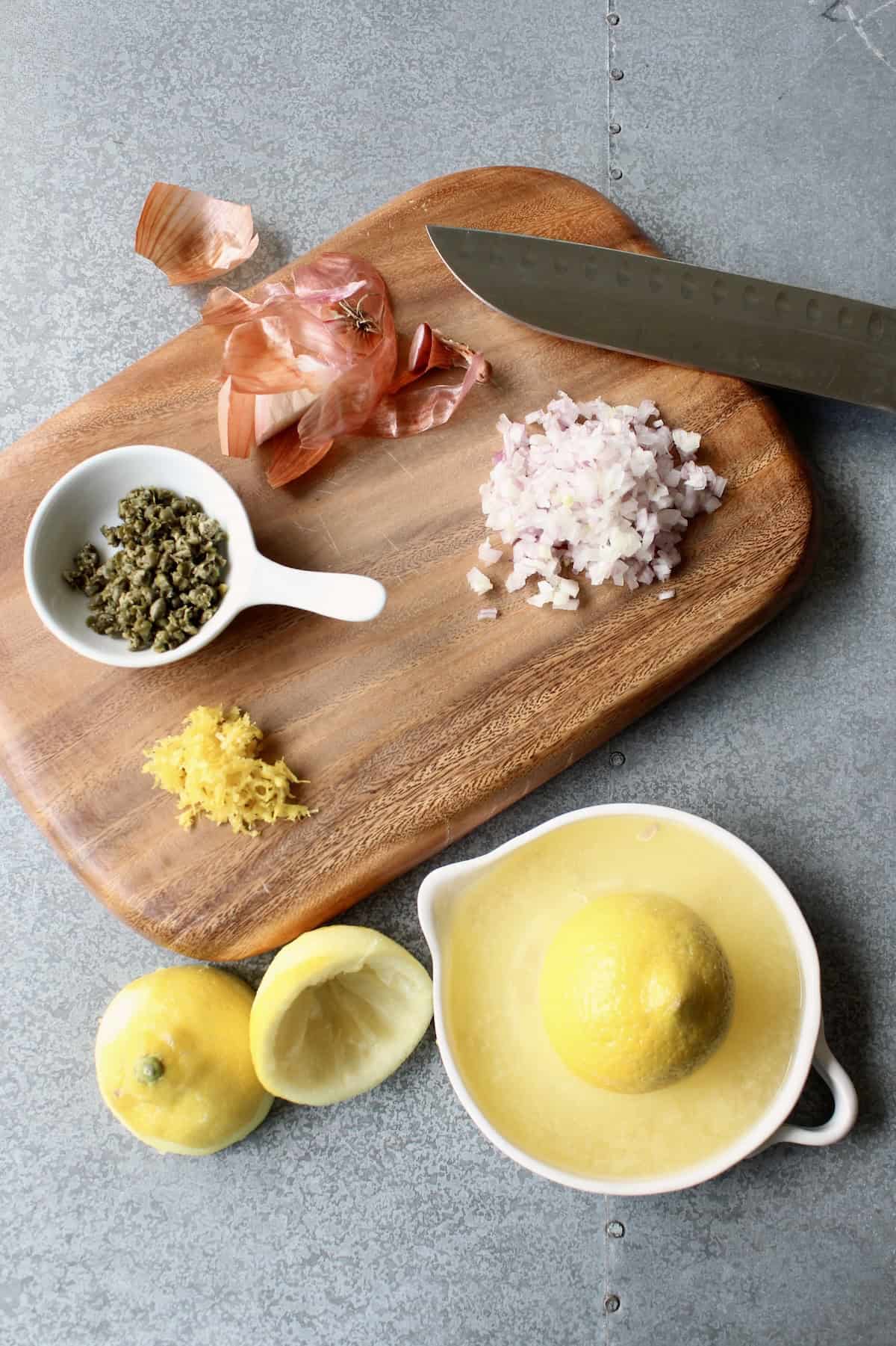 a wooden cutting board with lemons, capers, and shallots in various stages of preparation