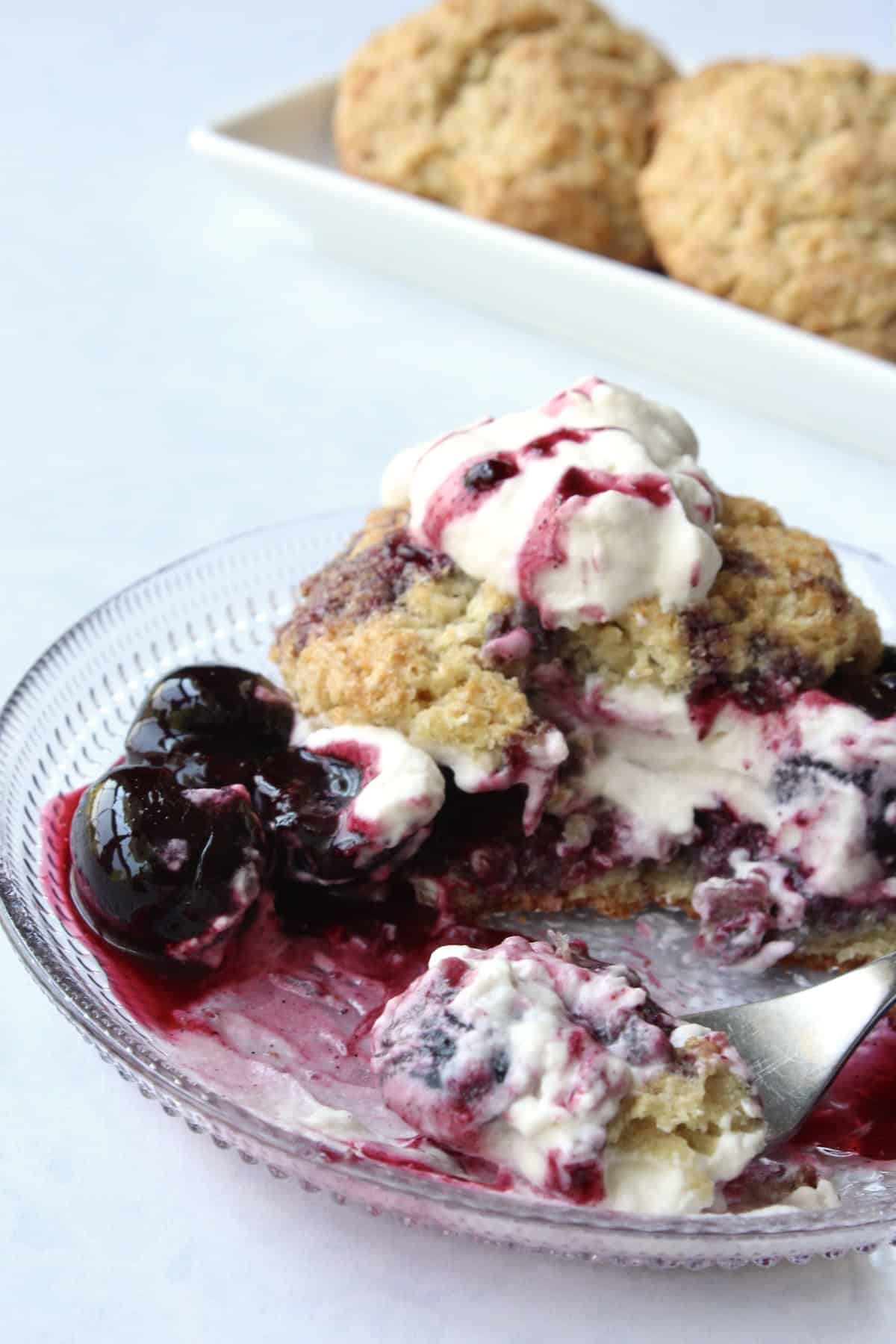 a partially eaten cherry shortcake is sliced into with a fork, cutting through layers of shortcake, cherries, and cream