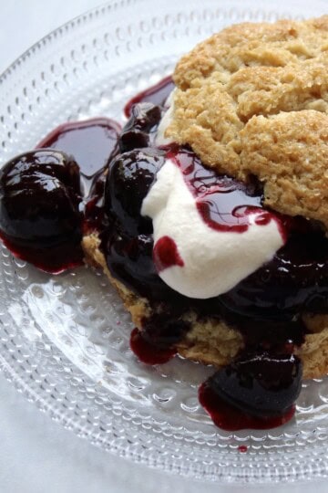 a plated cherry shortcake consists of cherry compote and whipped cream in between two layers of shortcake biscuit