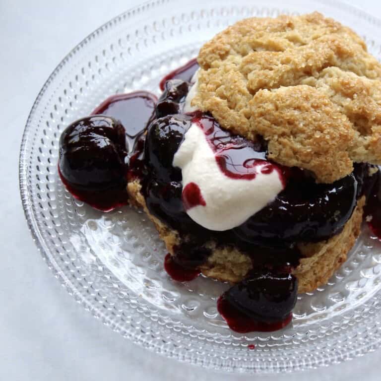 a plated cherry shortcake consists of cherry compote and whipped cream in between two layers of shortcake biscuit