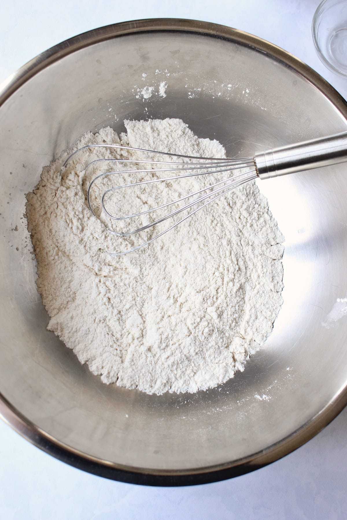 several different dry ingredients are whisked together in a metal mixing bowl.