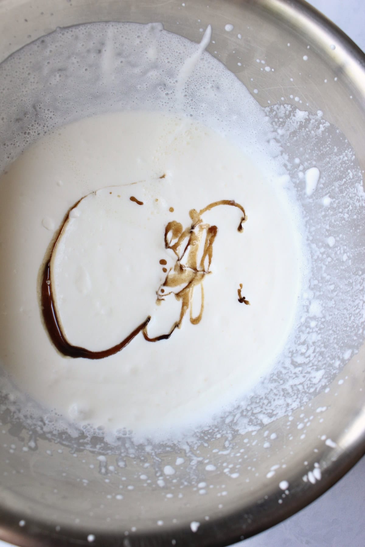 the brown sugar syrup is added to a mixing bowl of partially whipped heavy creamy
