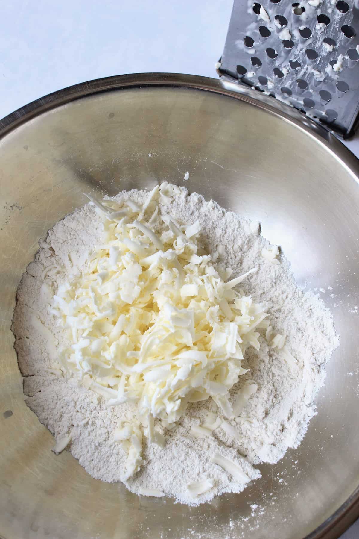 a pile of grated butter sits atop of a mixing bowl of dry ingredients
