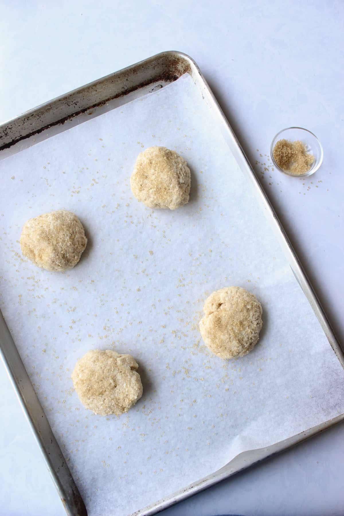 4 rounds of shortcake dough are arranged on a baking sheet and sprinkled with raw sugar