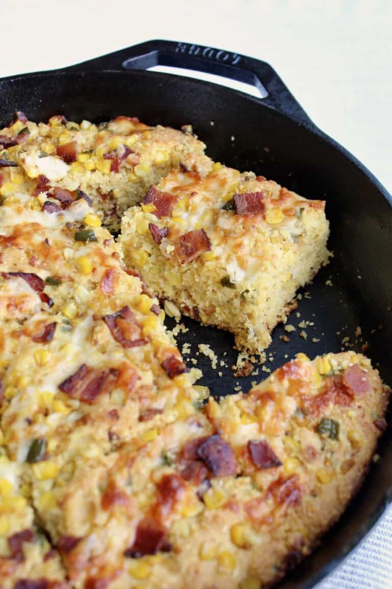 a slice of jalapeño bacon cornbread is pulled from the full cast iron skillet
