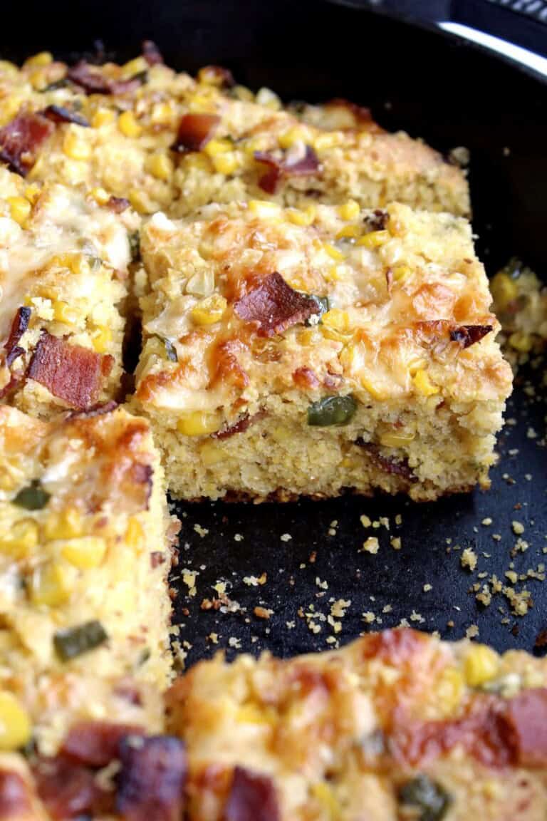 squares of jalapeño bacon cornbread in a cast iron skillet with one square missing